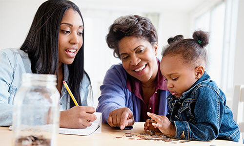 Three generations of women—grandmother, mother, and young daughter—counting coins together.