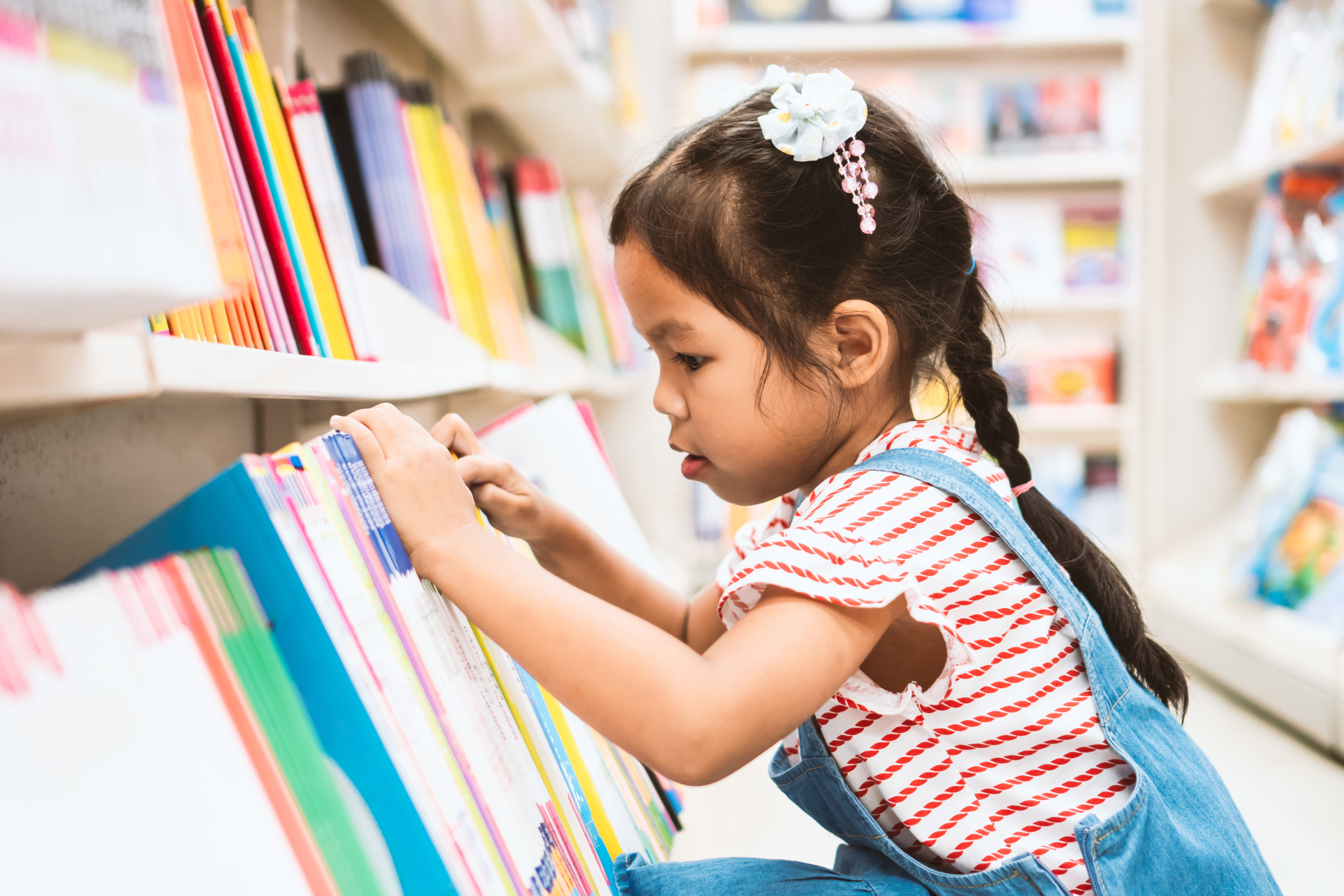 Child selecting a book from a library shelf.