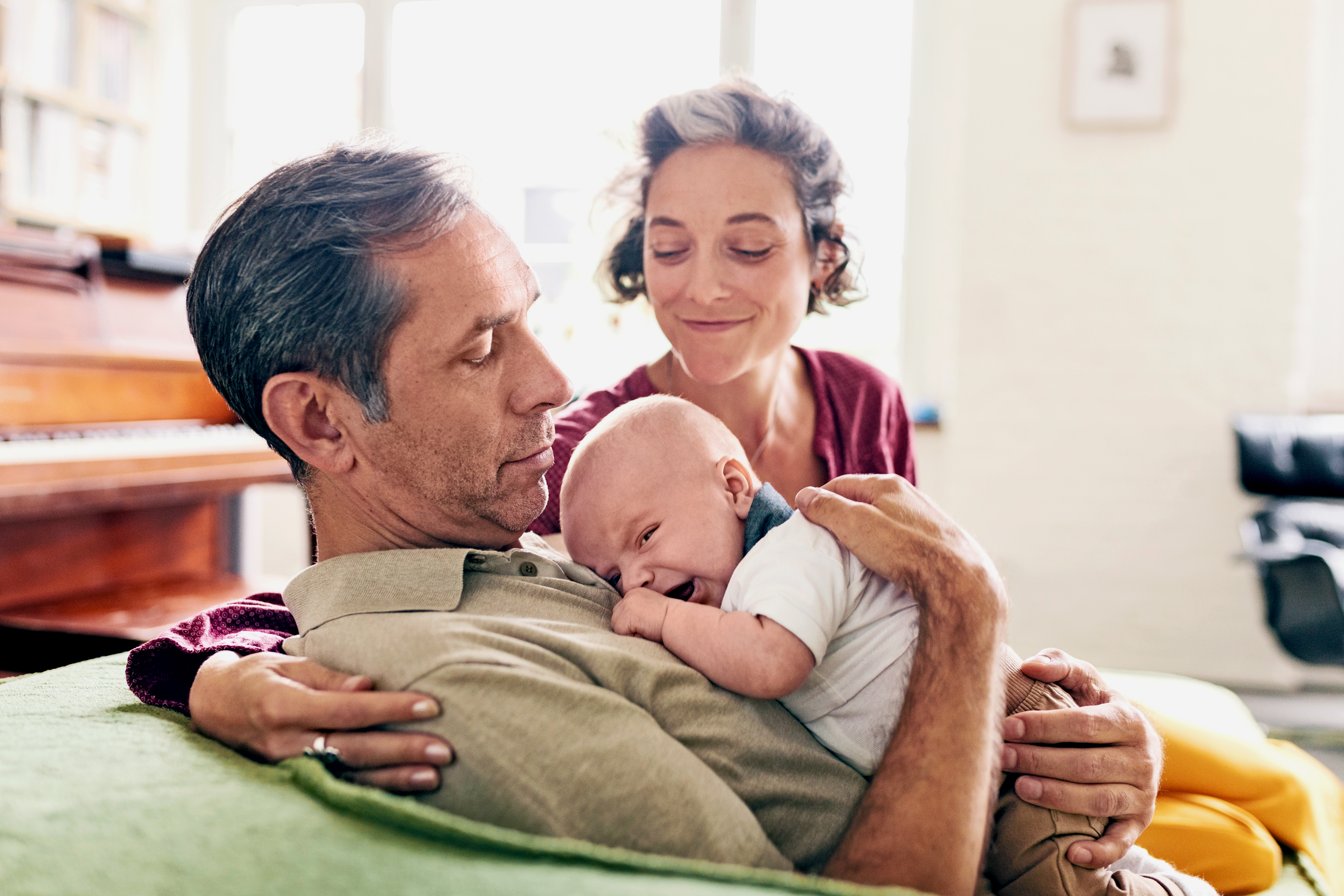 Grandfather holding baby grandchild while grandmother embraces them.